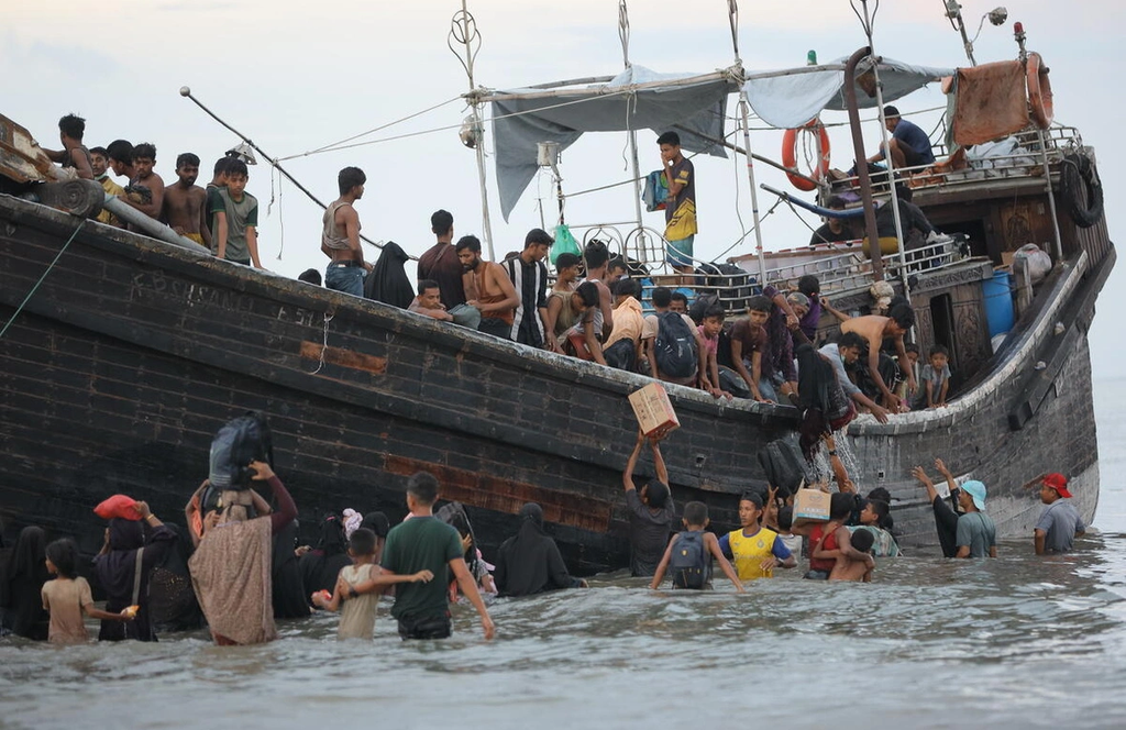 Rohingya refugees disembark from a crowded boat during a dangerous sea crossing in Southeast Asian waters.